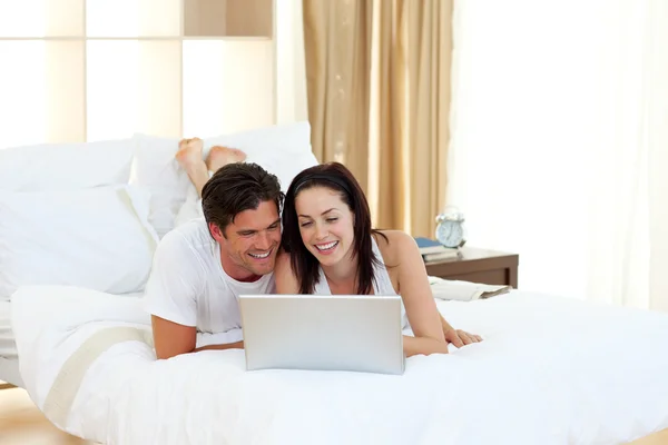 Lyckliga paret med en laptop liggande på deras säng — Stockfoto