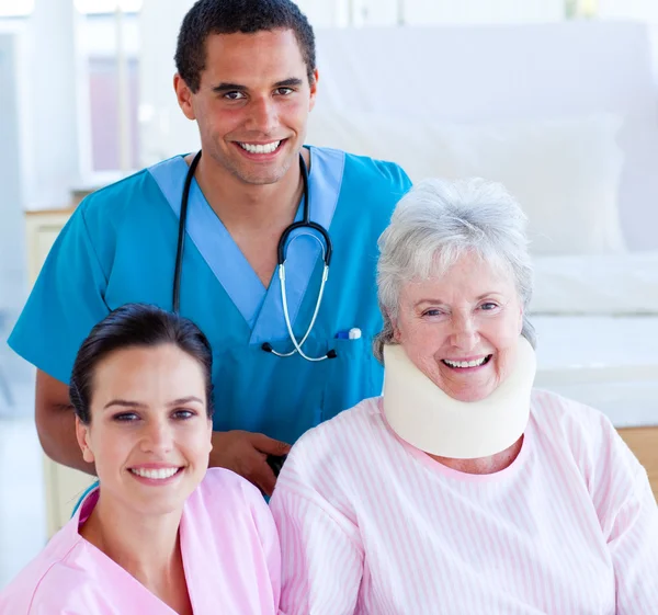 Zwei lächelnde Ärzte kümmern sich um eine verletzte Seniorin — Stockfoto