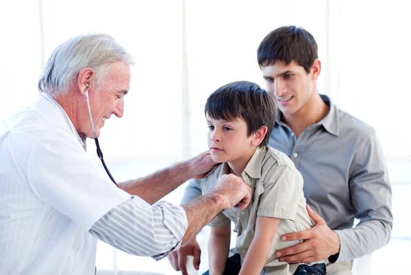 Старший врач осматривает маленького мальчика со своим отцом — стоковое фото