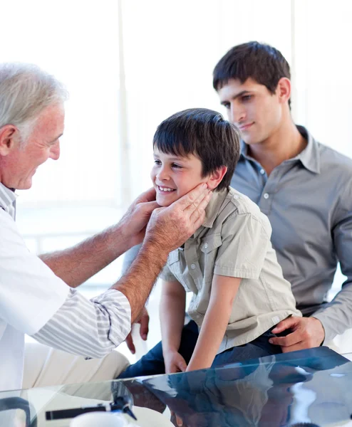 Старший врач осматривает горло маленького мальчика со своим отцом — стоковое фото