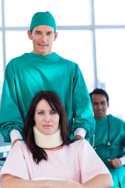 Atraktivní chirurg nesoucí pacienta na invalidní vozík — Stock fotografie