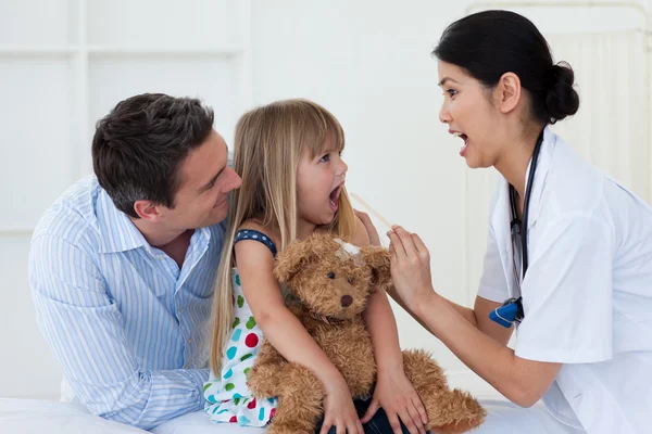 Маленькая девочка открывает рот и доктор проверяет ее горло — стоковое фото
