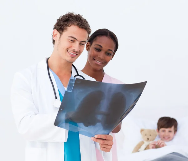 Pediatrician and nurse examining an x-ray and a little patient i — Stock Photo, Image