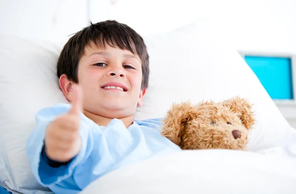 Μικρό αγόρι αγκαλιάζει ένα αρκουδάκι που βρίσκεται σε ένα κρεβάτι του στο νοσοκομείο — Φωτογραφία Αρχείου