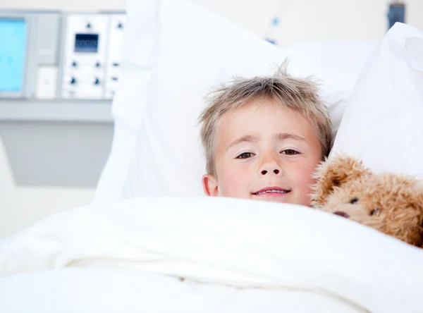 Больной очаровательный маленький мальчик лежит на больничной койке со своим плюшевым мишкой — стоковое фото