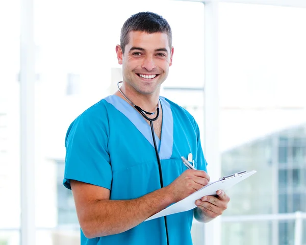 Усміхнений чоловічий лікар робить нотатки в папці пацієнта — стокове фото