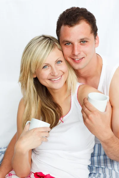 Ζευγάρι στο κρεβάτι πίνοντας καφέ και να χαμογελά στη φωτογραφική μηχανή — Φωτογραφία Αρχείου