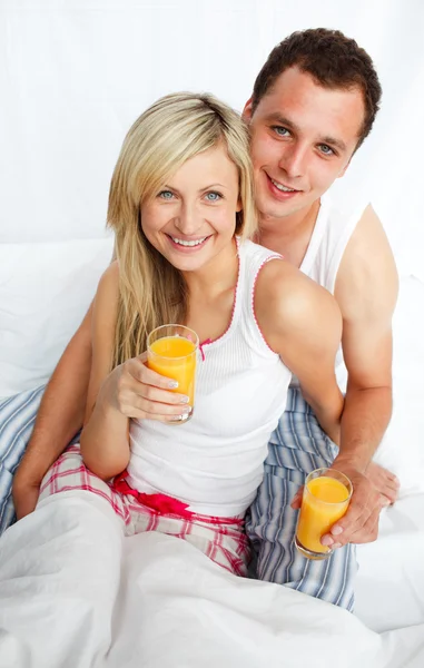 Casal segurando copos de suco de laranja na cama — Fotografia de Stock