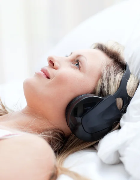 Smiling woman with headphones on lying on a bed — Stock Photo, Image