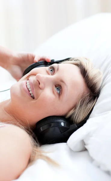 Mulher encantadora com fones de ouvido em deitado em uma cama — Fotografia de Stock