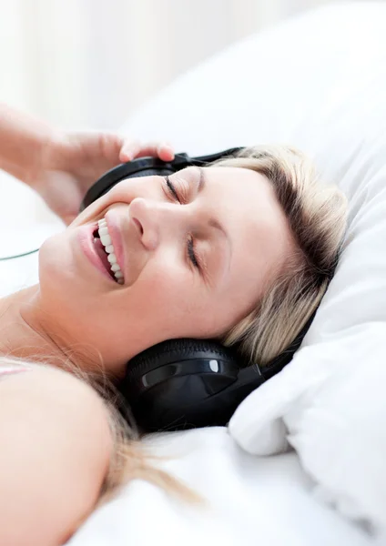 Mulher entusiasmada com fones de ouvido deitada em uma cama — Fotografia de Stock