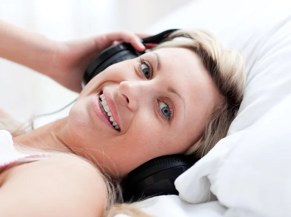 Mulher positiva com fones de ouvido em deitado em uma cama — Fotografia de Stock