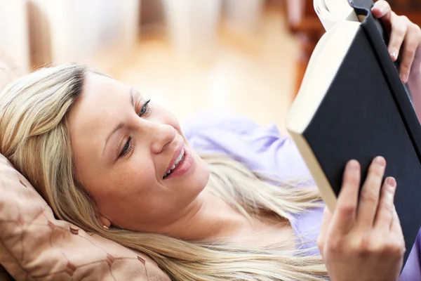 Vrolijke vrouw lezen van een boek liggen op een sofa — Stockfoto