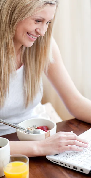 Glad kvinna använder en bärbar dator samtidigt ha en frukost — Stockfoto