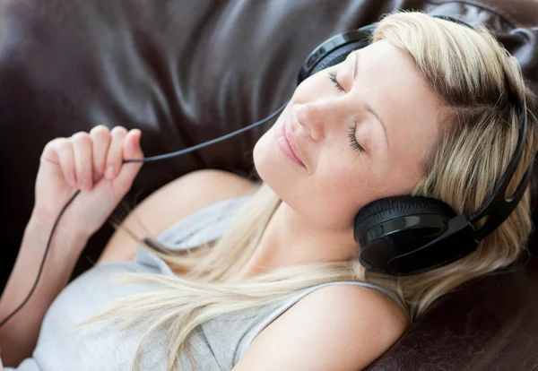 Mulher relaxada com fones de ouvido em deitado em um sofá — Fotografia de Stock