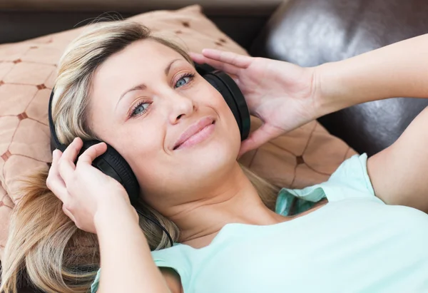 Χαμογελώντας η γυναίκα με τα ακουστικά για ξαπλωμένη σε ένα καναπέ — Φωτογραφία Αρχείου