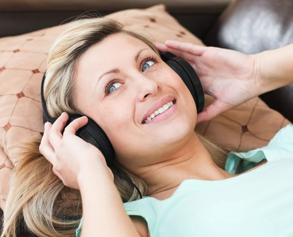 Mulher alegre com fones de ouvido em deitado em um sofá — Fotografia de Stock