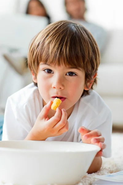 Beautiful little boy eating chips lying on the floor — Stock Photo, Image
