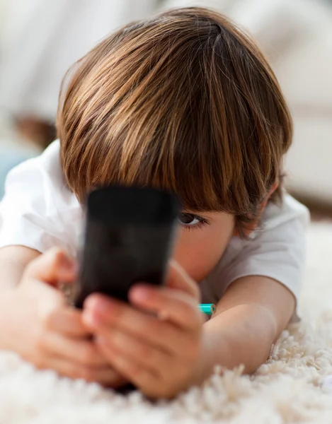 Adorable little boy holding a remote lying on the floor — Stock Photo, Image