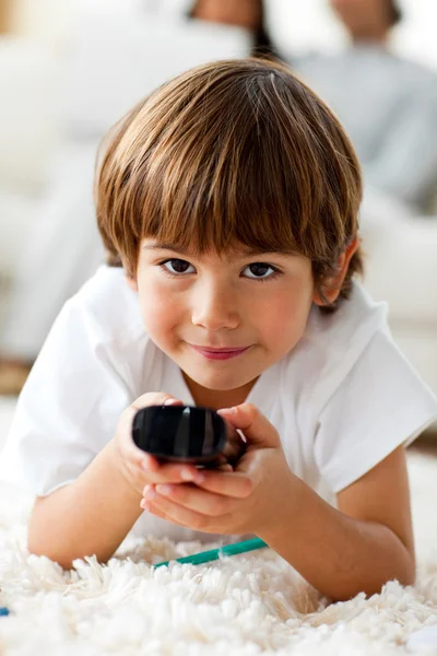 Niño sonriente sosteniendo un control remoto tirado en el suelo —  Fotos de Stock