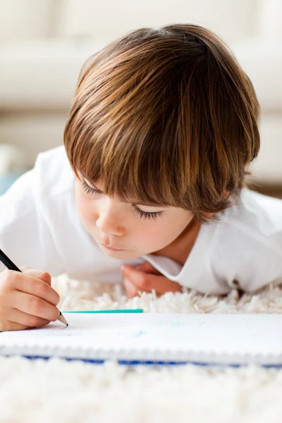 Серьезный маленький мальчик рисует лежа на полу — стоковое фото