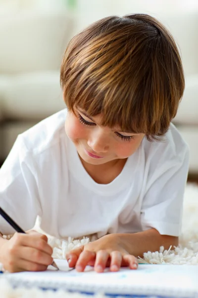 Веселый маленький мальчик, рисующий лежа на полу — стоковое фото