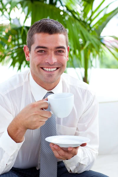 Businessman drinking a cup of coffee on a sofa in workplace — Stock Photo, Image