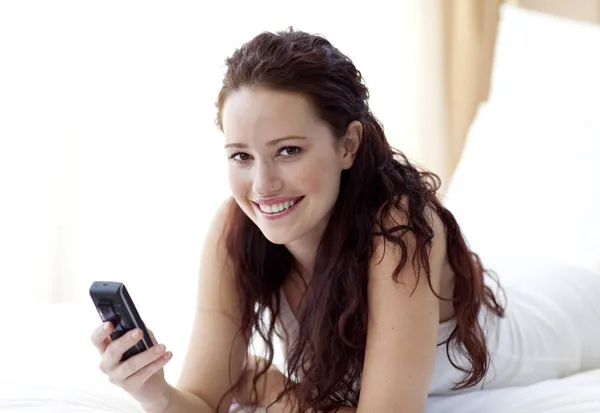 Smilende kvinne sender en sms i senga – stockfoto
