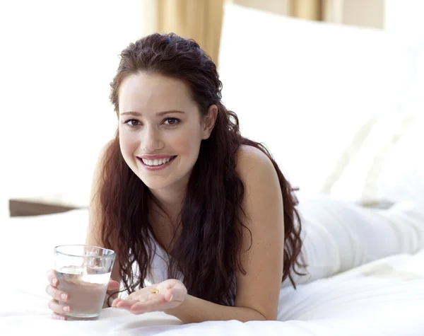 Mulher na cama tomando pílulas com água — Fotografia de Stock