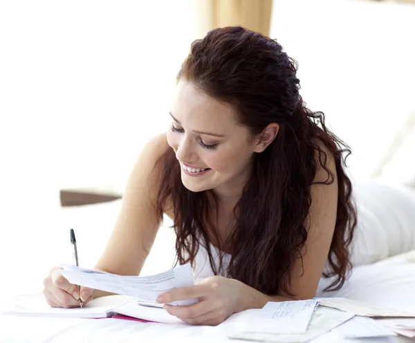 Smiling woman writing notes in bed — Stock Photo, Image
