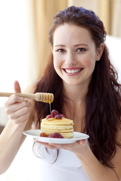 Smiling woman eating pancakes with fruit and honey — Stock Photo, Image