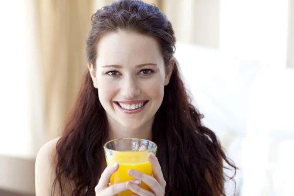 Девушка пьет апельсиновый сок в спальне — стоковое фото