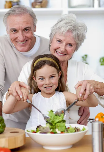 Улыбающиеся бабушка и дедушка едят салат с внучкой — стоковое фото