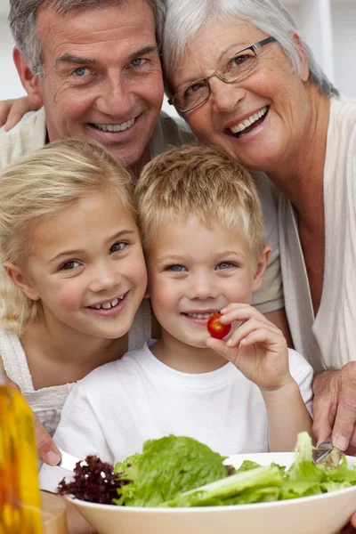 Счастливые бабушка и дедушка едят салат с внуками — стоковое фото
