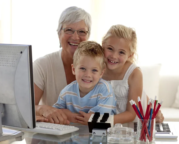 Happy children using a computer with their grandmother — Stock Photo, Image
