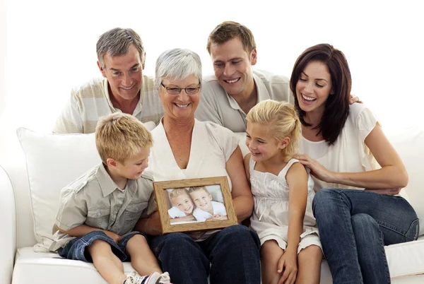 Happy family holding a portrait of children sitting on sofa — Stock Photo, Image