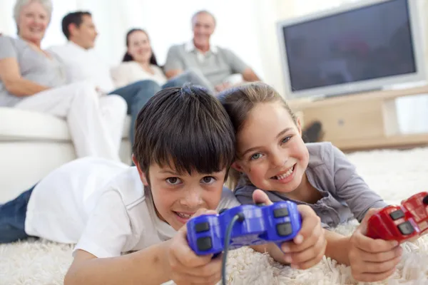 Παιδιά που παίζουν βιντεοπαιχνίδια στον όροφο και οικογένεια στον καναπέ — Φωτογραφία Αρχείου