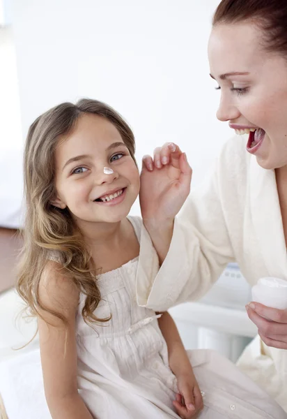 Happy mother putting cream on her daughter's face — Stock Photo, Image