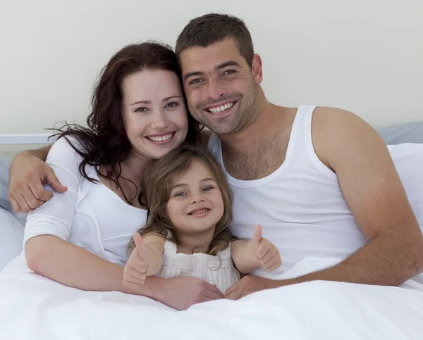 Jovem família feliz na cama com os polegares para cima — Fotografia de Stock