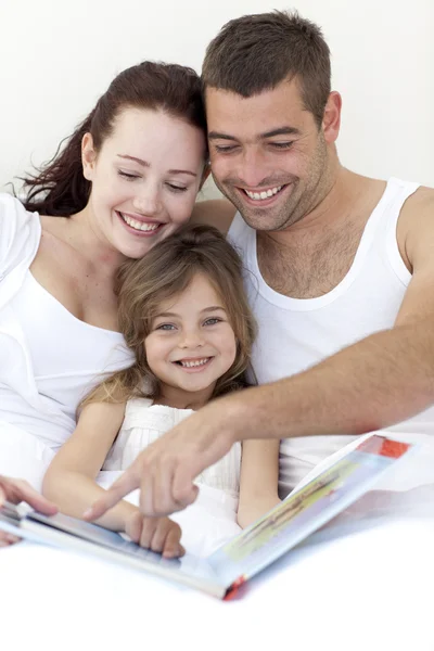 Portrait of a girl reading with her parents in bed — Stock Photo, Image