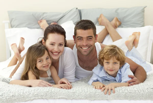 Glückliche Familie liegt im Bett und lächelt in die Kamera — Stockfoto
