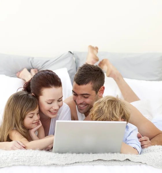 Eltern und Kinder spielen im Bett mit einem Laptop — Stockfoto