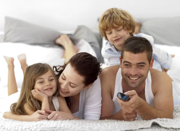 Familie liegt im Bett und benutzt eine Fernbedienung — Stockfoto