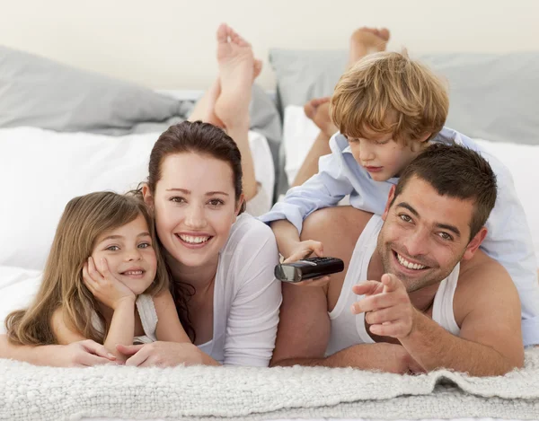 Família relaxando na cama e usando um controle remoto — Fotografia de Stock