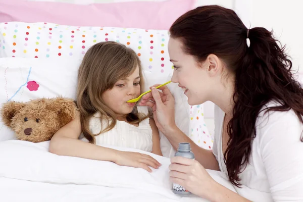 Маленькая девочка в постели принимает сироп — стоковое фото