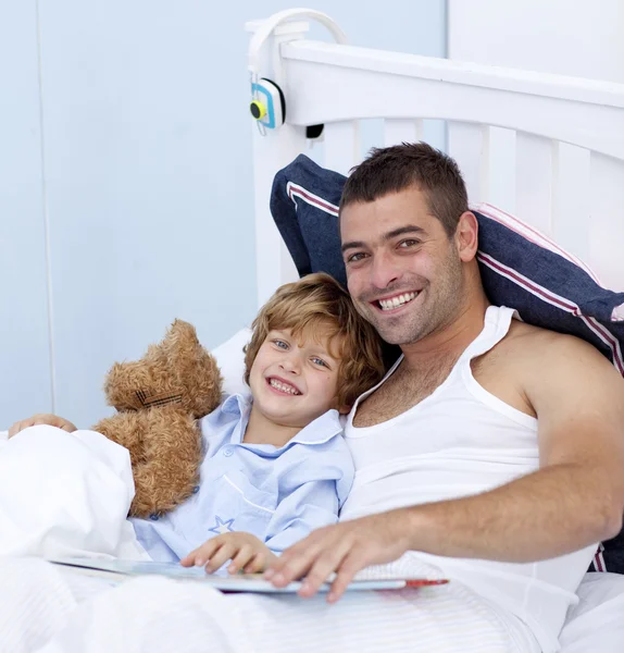 Smiling father and son reading a book in bed — Stock Photo, Image