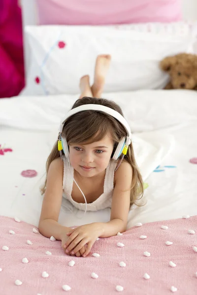 头戴式耳机听听音乐在床上的小女孩 — 图库照片