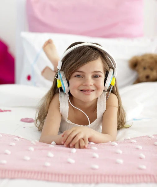 头戴式耳机听听音乐在床上的小女孩 — 图库照片