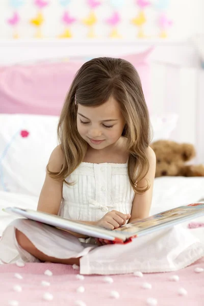 小女孩坐在床上读一本书 — 图库照片