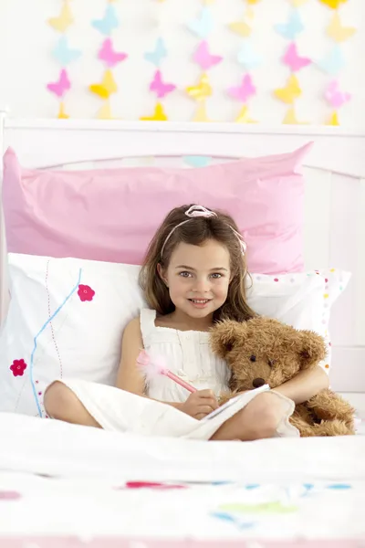 Smiling little girl writing in bed — Stock Photo, Image